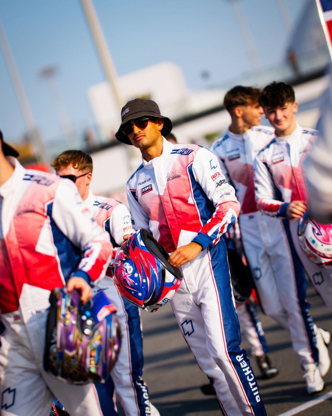 Team UK driver in a bucket hat carries his helmet