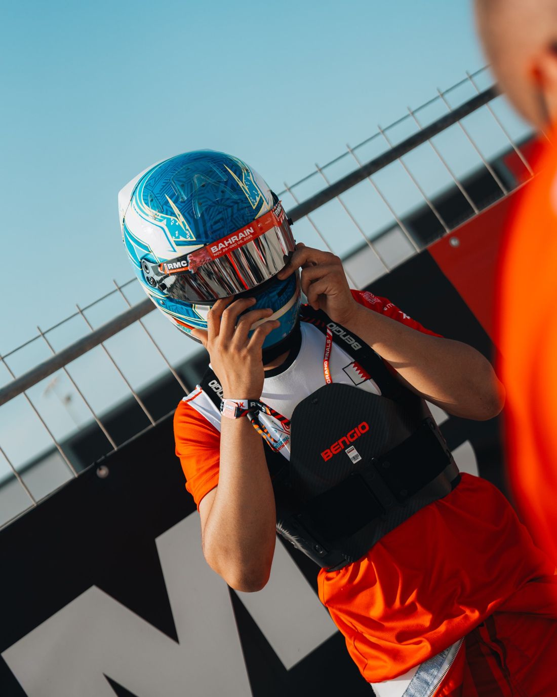 Driver pulls on a blue helmet by the fence