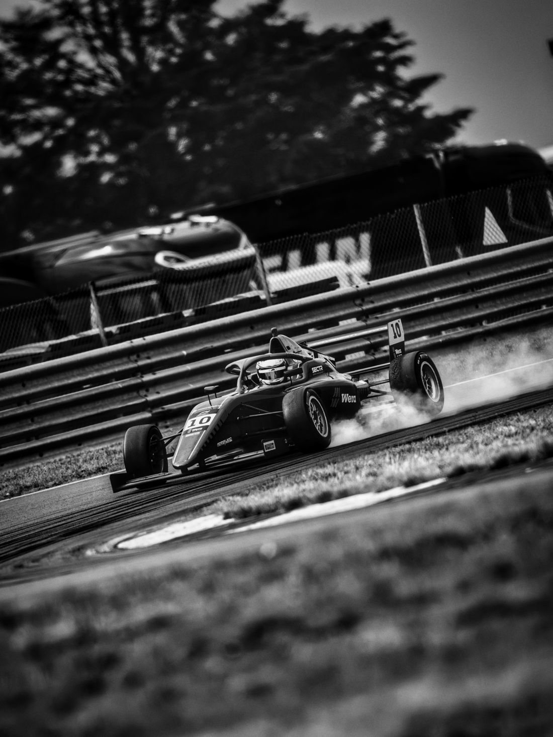 Car number 10 locks up in a cloud of tyre smoke, black and white