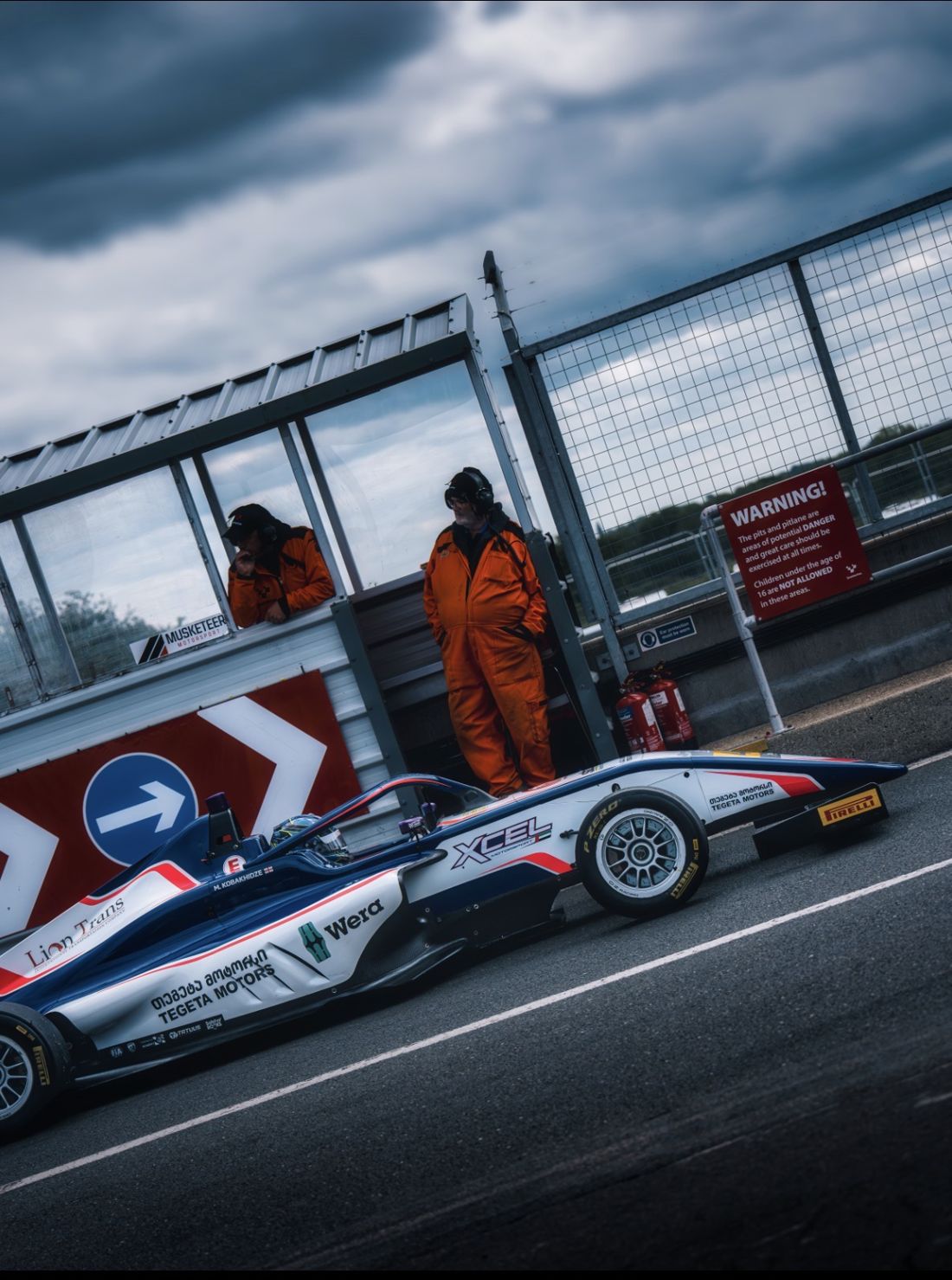 Xcel car waits in the pit lane under storm clouds